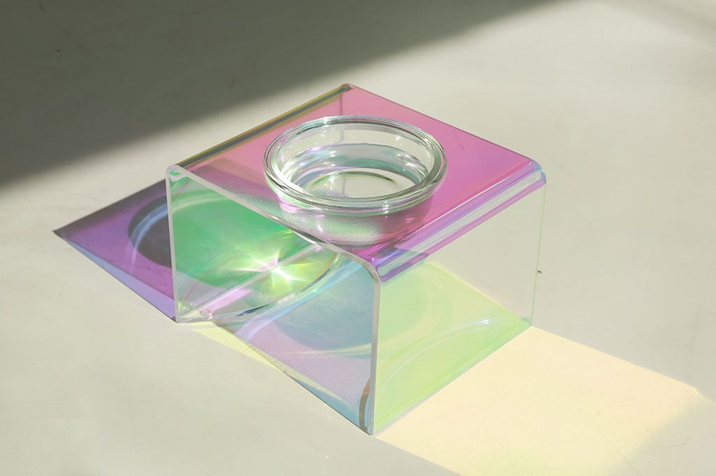 Iridescent glass bowl on colorful geometric stand with rainbow reflections
